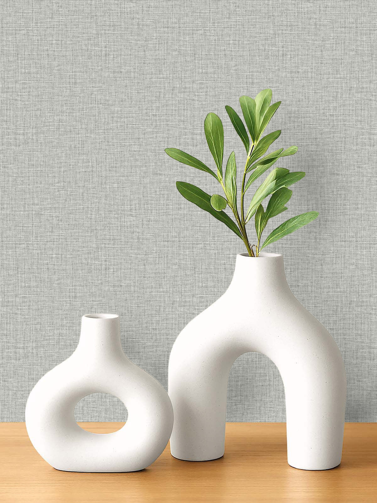Two white ceramic vases on wood, set against washable, textured gray Pearly Linen Wallpaper.