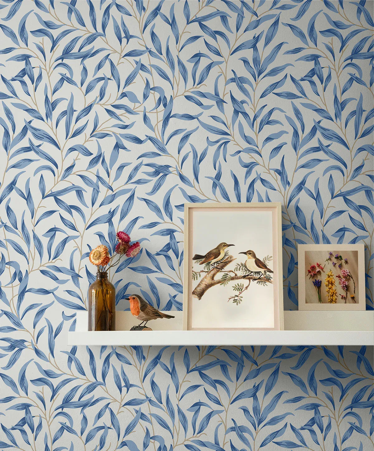 White shelf on Leafy Branches Peel Stick wallpaper with bird art, framed flowers, a brown vase, and bird figurine.