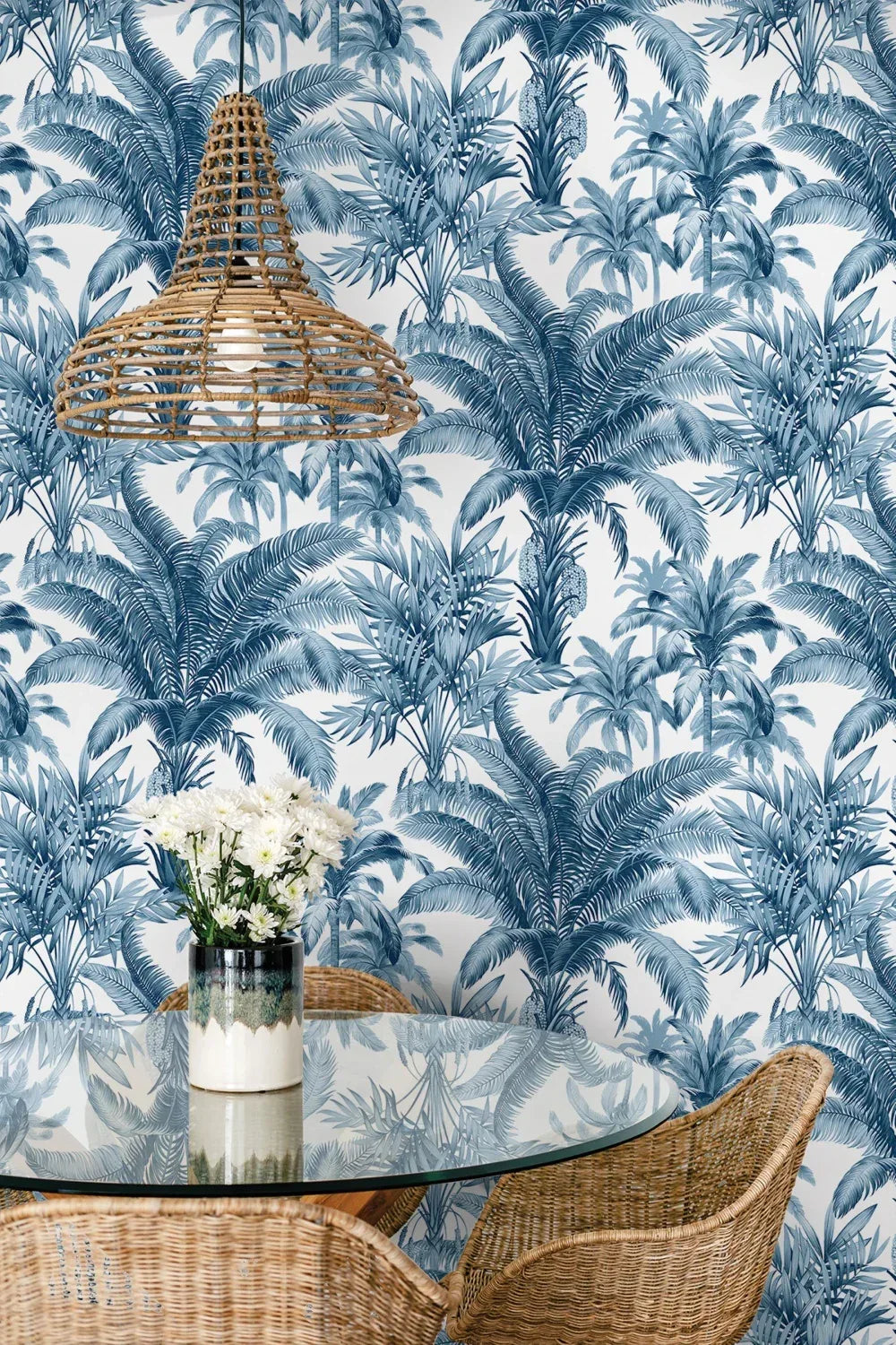 Rattan chairs and lamp beside a glass table with flowers, set against Palm Grove Peel Stick wallpaper.