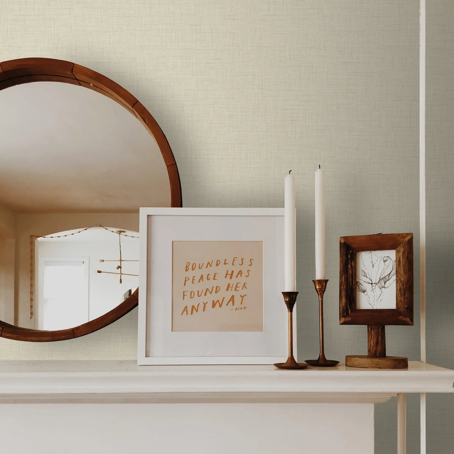 A round mirror, framed art, and candles sit on a mantel against warm beige Linen Texture Commercial Vinyl wallcovering.