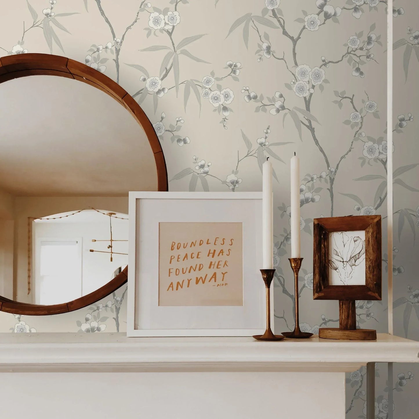 Round mirror, framed quote, candles, and small art on a white mantle with Blossom Spring Flower Wallpaper.