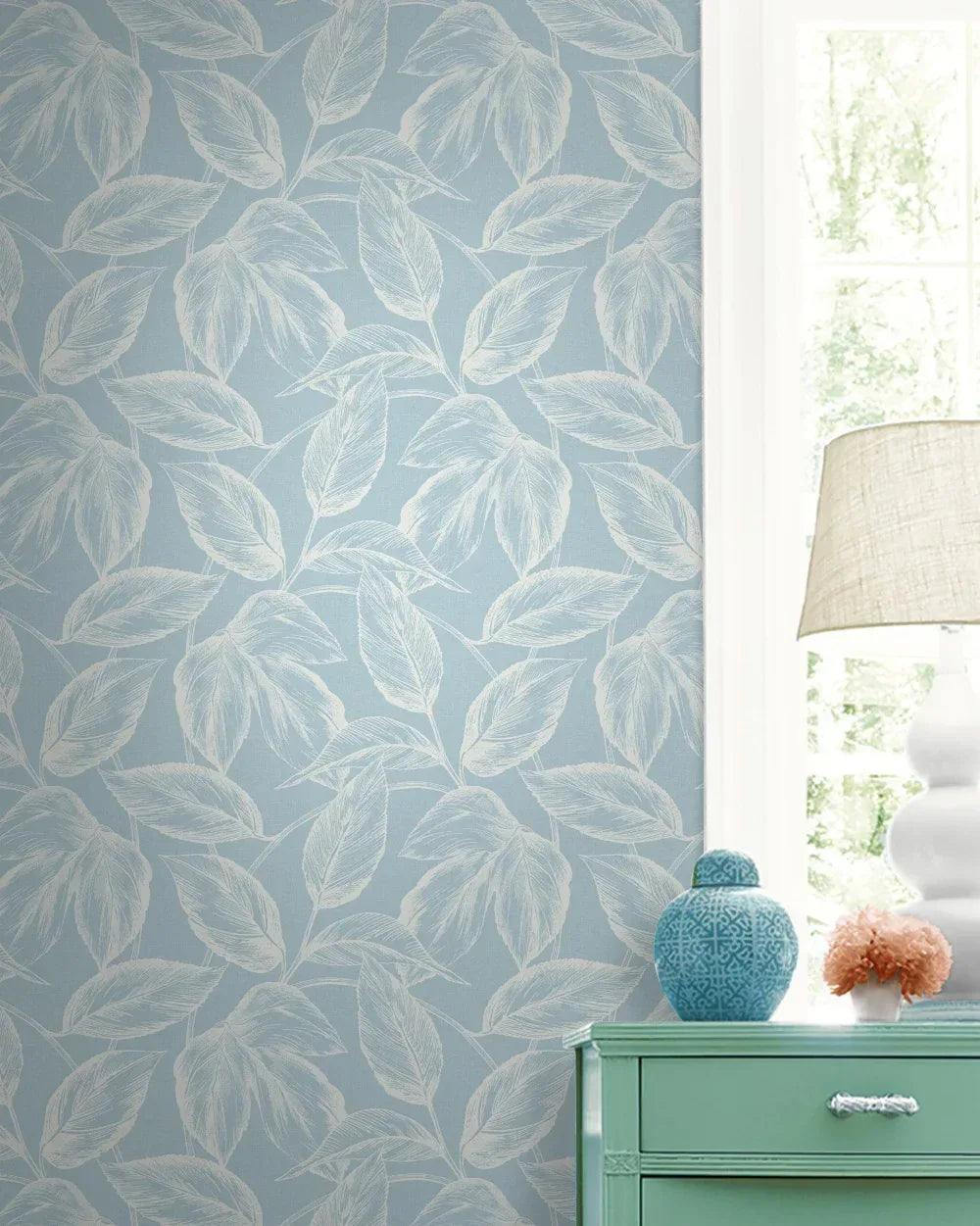 Sketched Leaves Wallpaper in light blue with white leaf pattern, styled with a window, lamp, blue vase, and mint table.