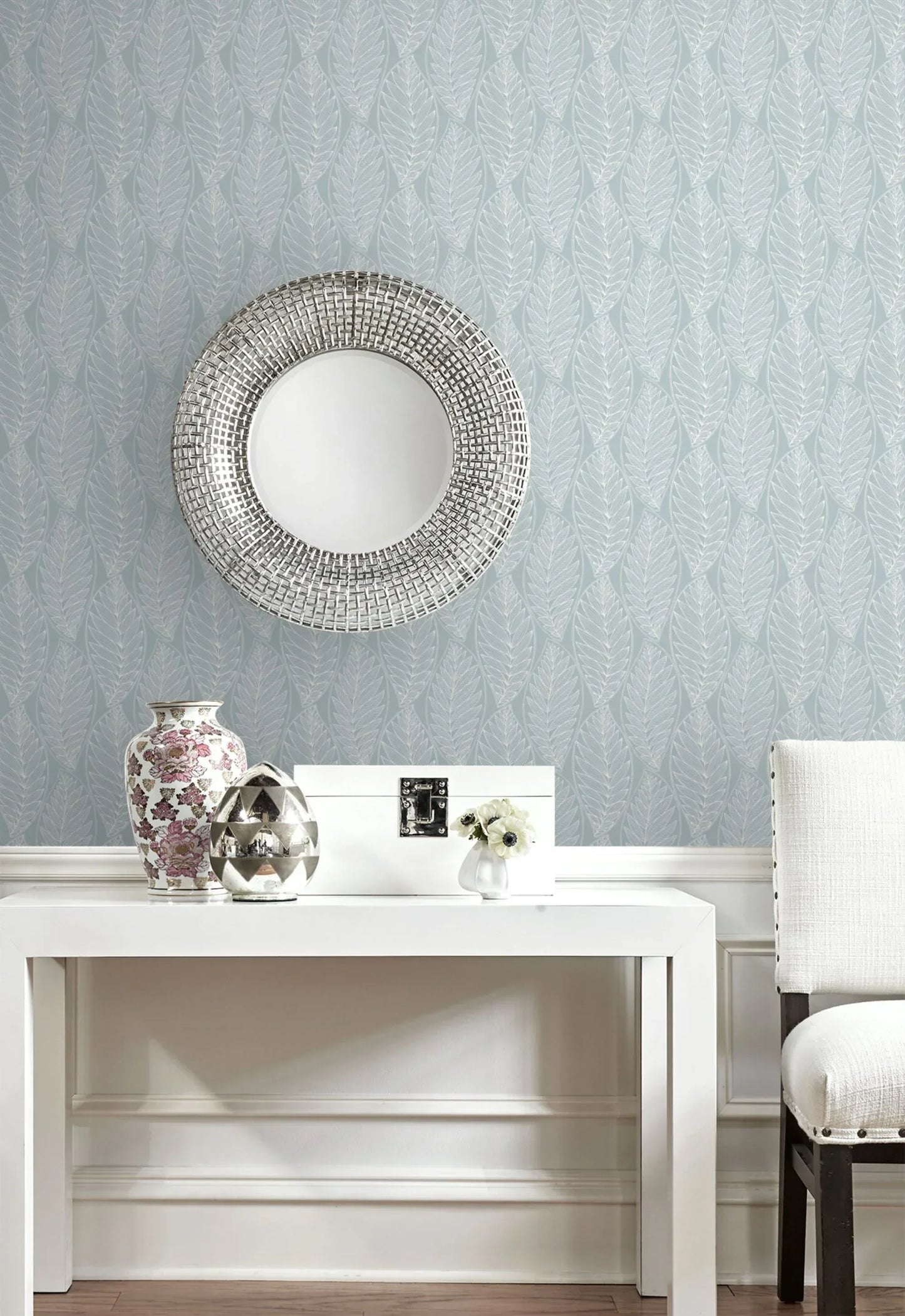 Round mirror above white table with vases, flower, and chair beside Kira Leaf Wallpaper.
