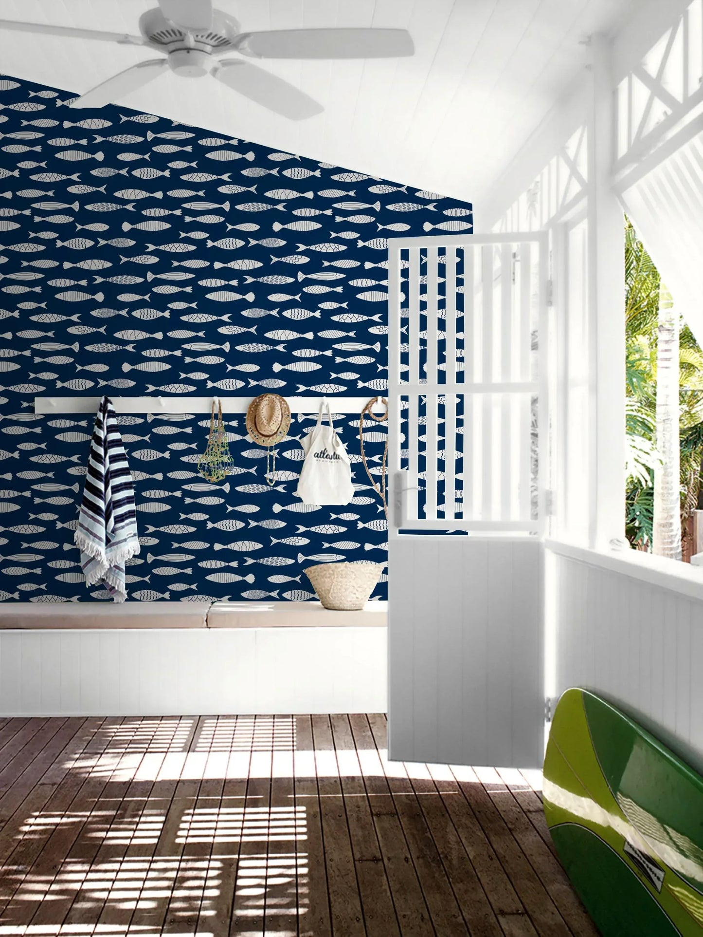 A bright room with Painted Fish Wallpaper, beach hats, striped towels, and a surfboard by an open window.