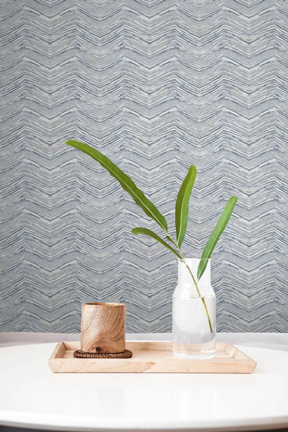 A tray with a cup and vase sits on a white table, backed by Wood Chevron Peel Stick wallpaper.