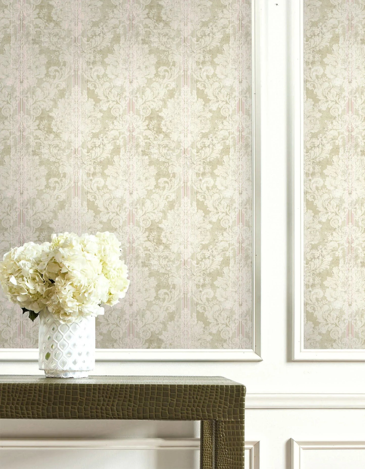 White hydrangeas in a textured vase on a table with Vintage Damask Wallpaper and a white paneled wall.