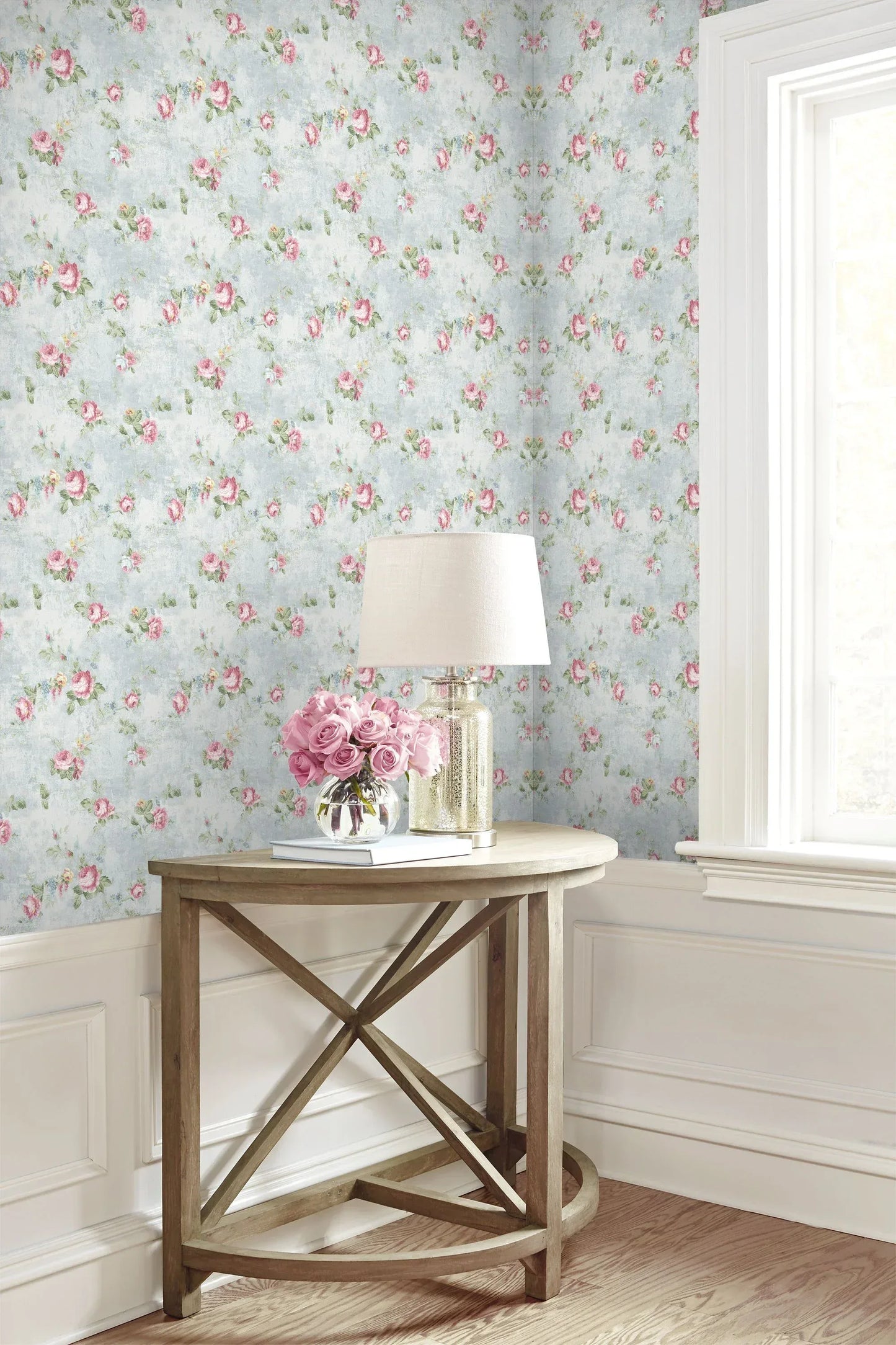 Wooden table with a lamp and pink flowers, set against English Flowers Wallpaper for a countryside vibe.