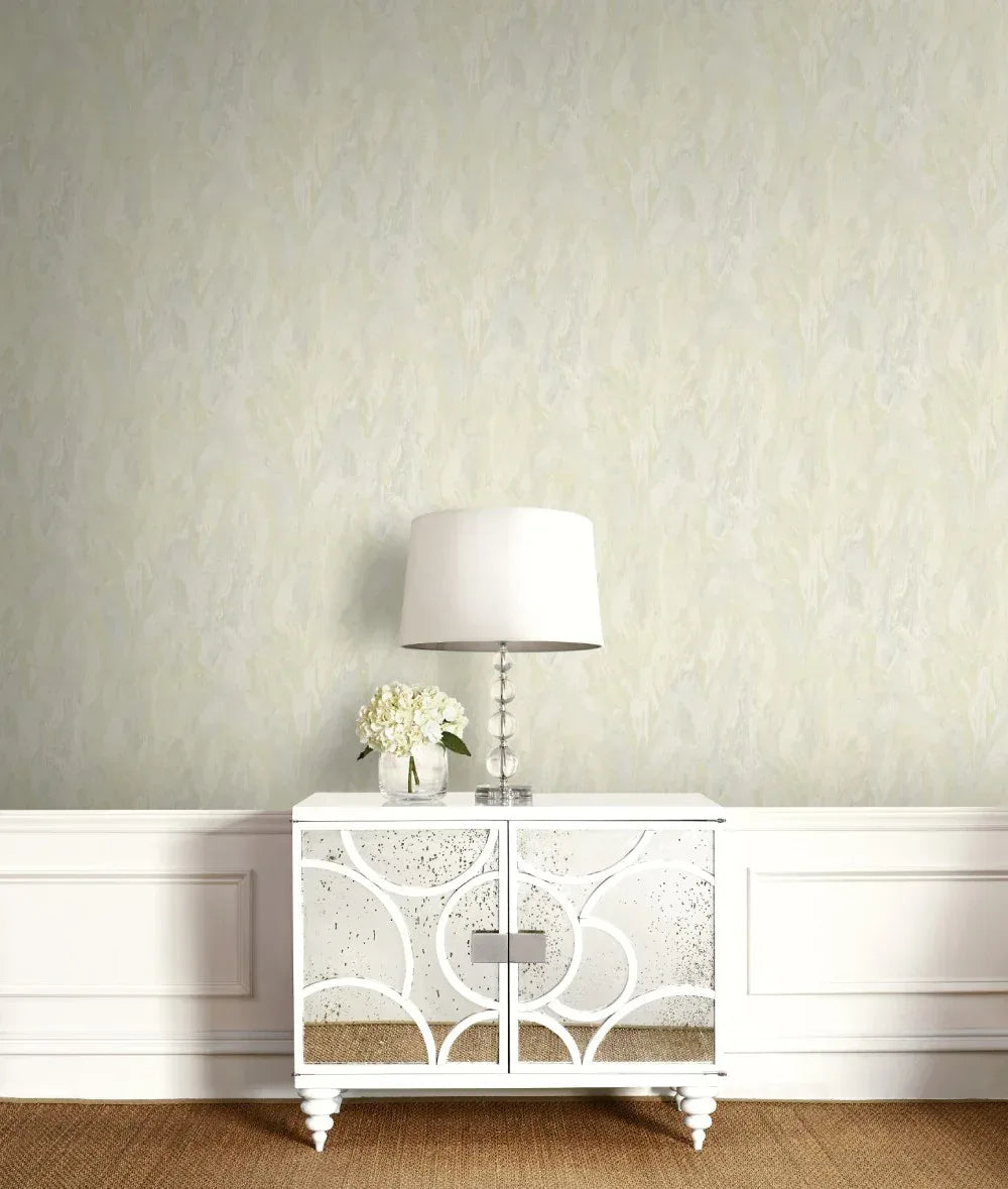 A white mirrored console table with a lamp and flowers stands against Veined Marble Wallpaper and white wainscoting.