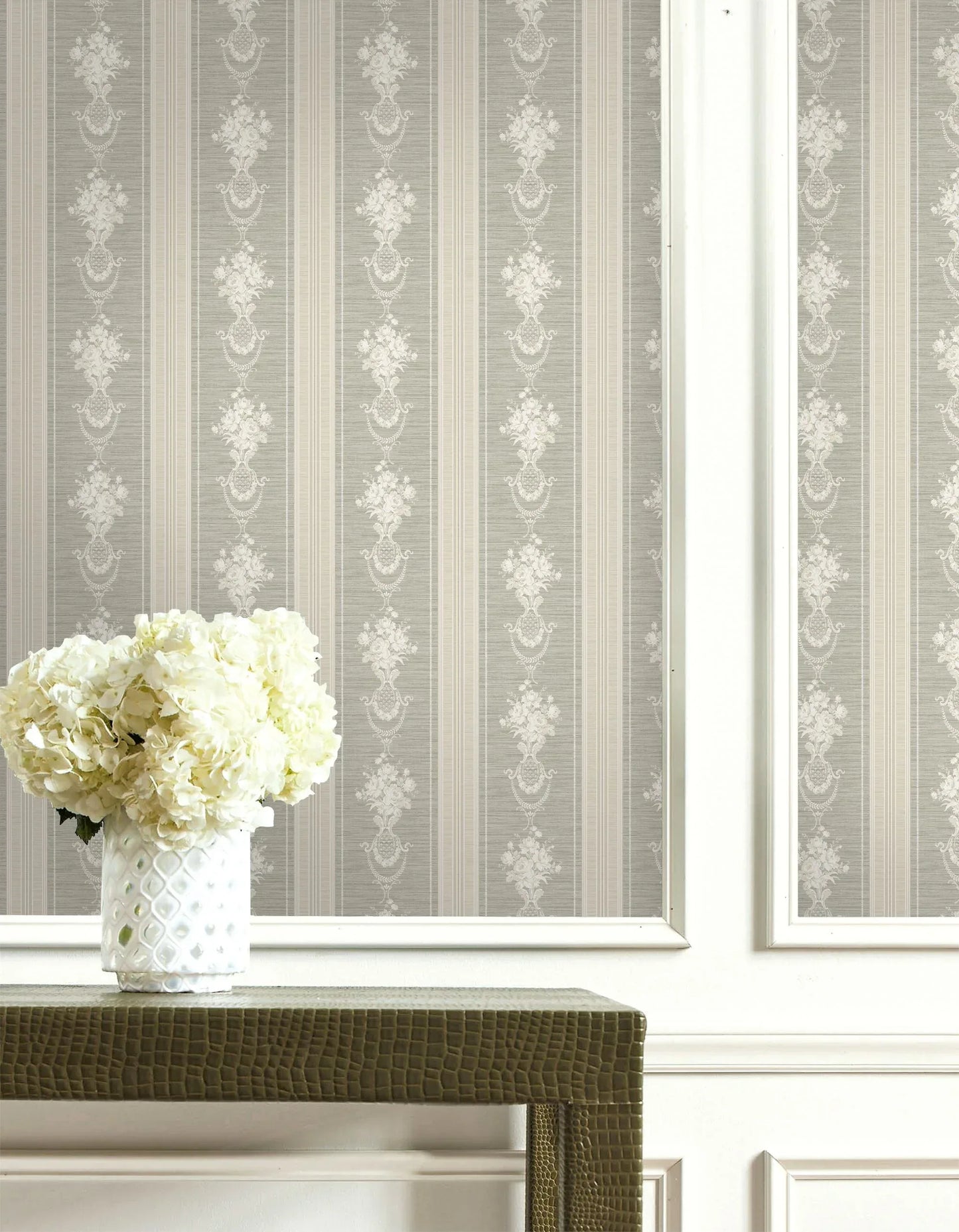 A vase of white hydrangeas sits on a textured table before elegant beige Floral Cameo Stripe Wallpaper.