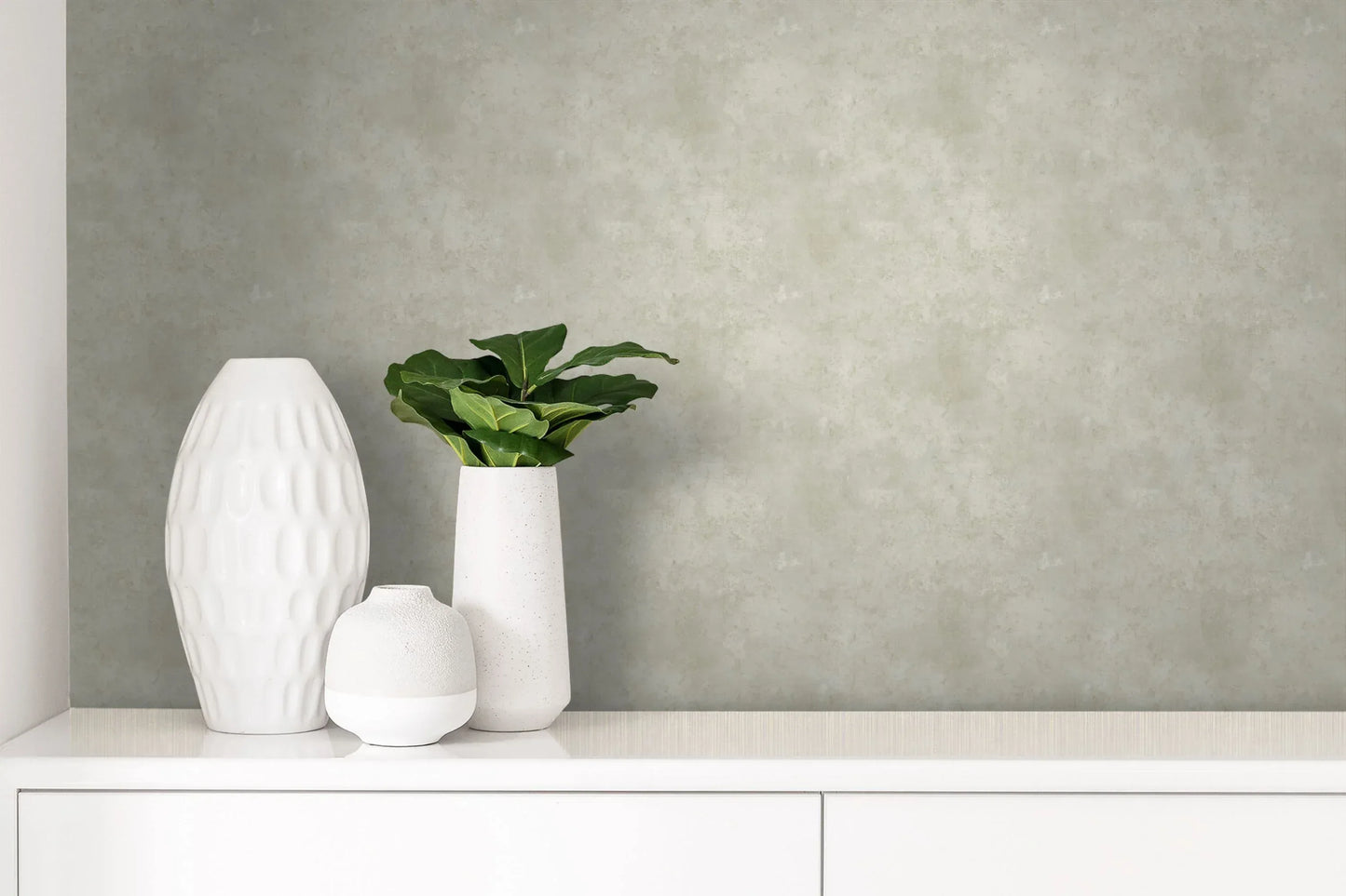 Three vases and a small plant on a white cabinet with Marble Carrara Wallpaper in the background.
