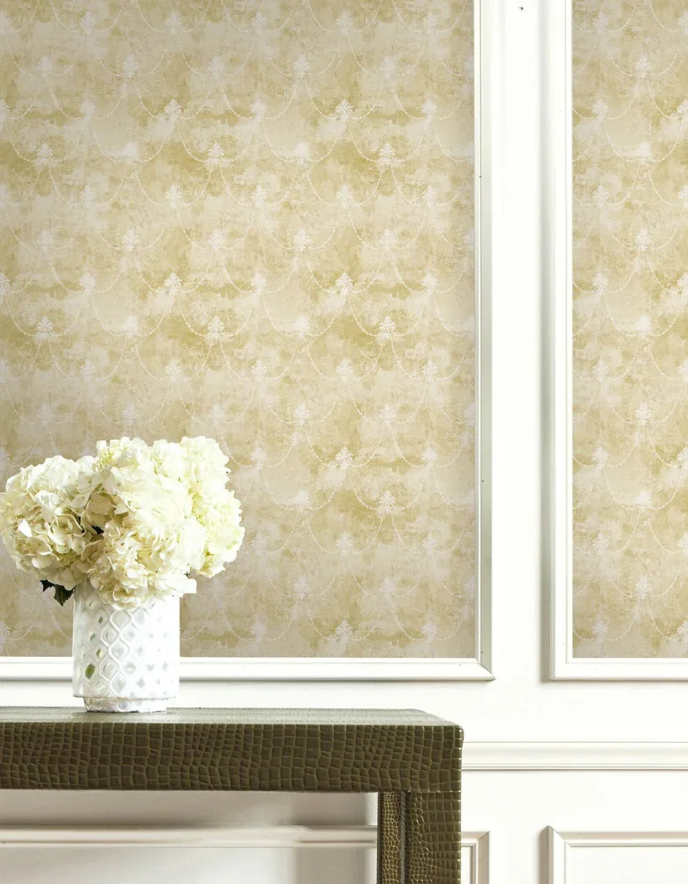 A vase of white flowers sits on a textured table before beige Lys Flower Wallpaper with white trim.