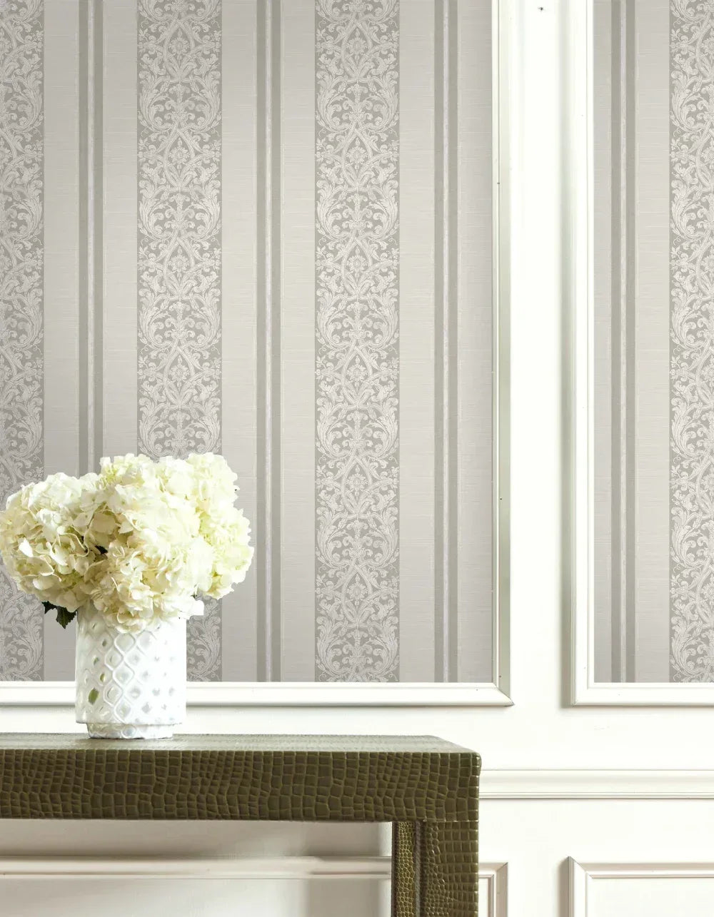 White hydrangeas in a textured vase on a table, set against elegant gray and white Gothic Stripes Wallpaper.