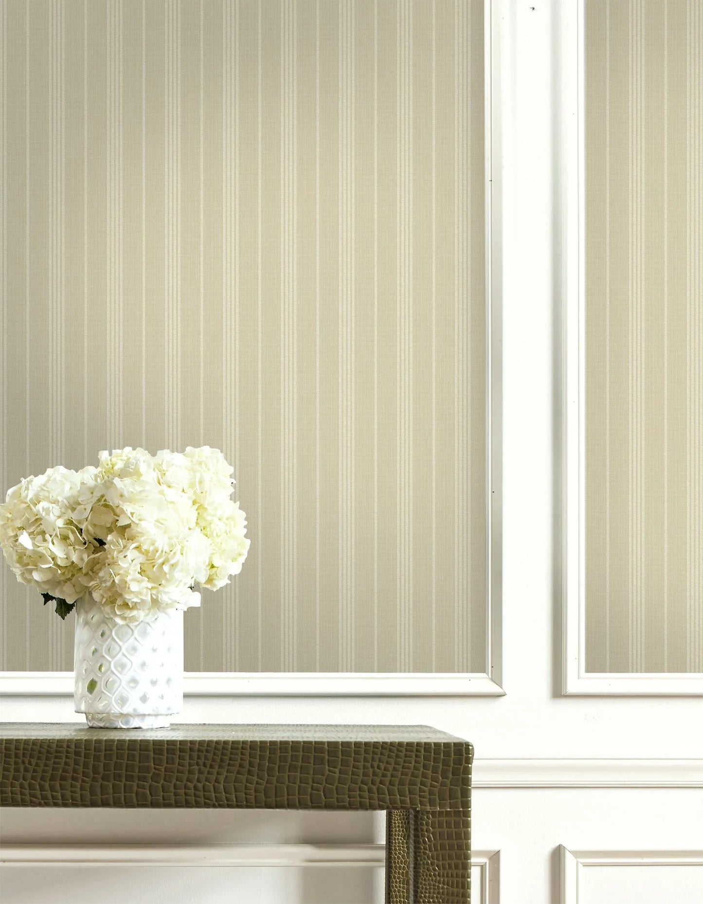 A white vase with white hydrangeas sits on a green table against Classic Stripe wallpaper and white paneling.