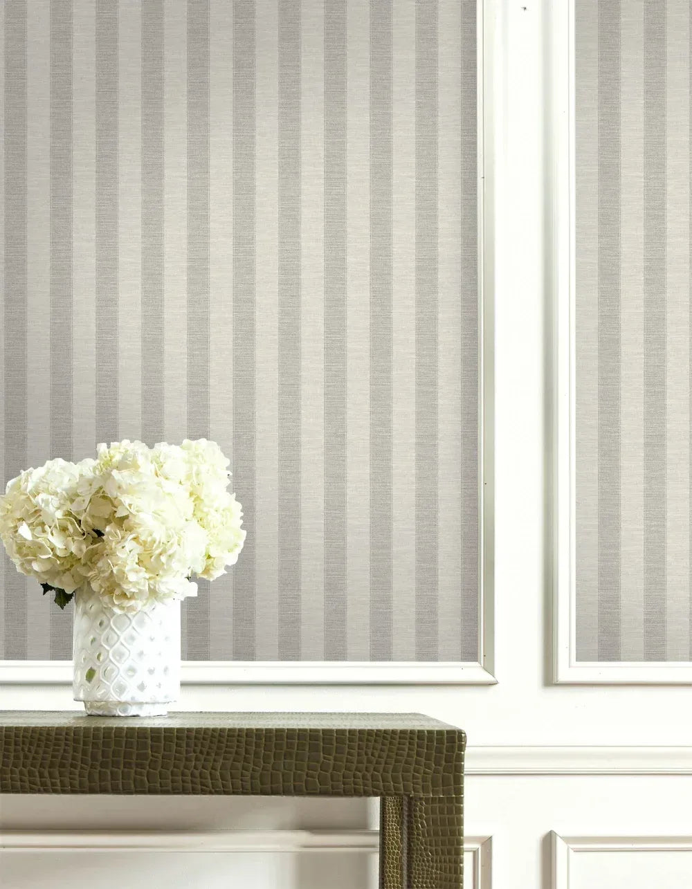 A white vase with flowers sits on a textured table against Textile Stripe Wallpaper with white trim.