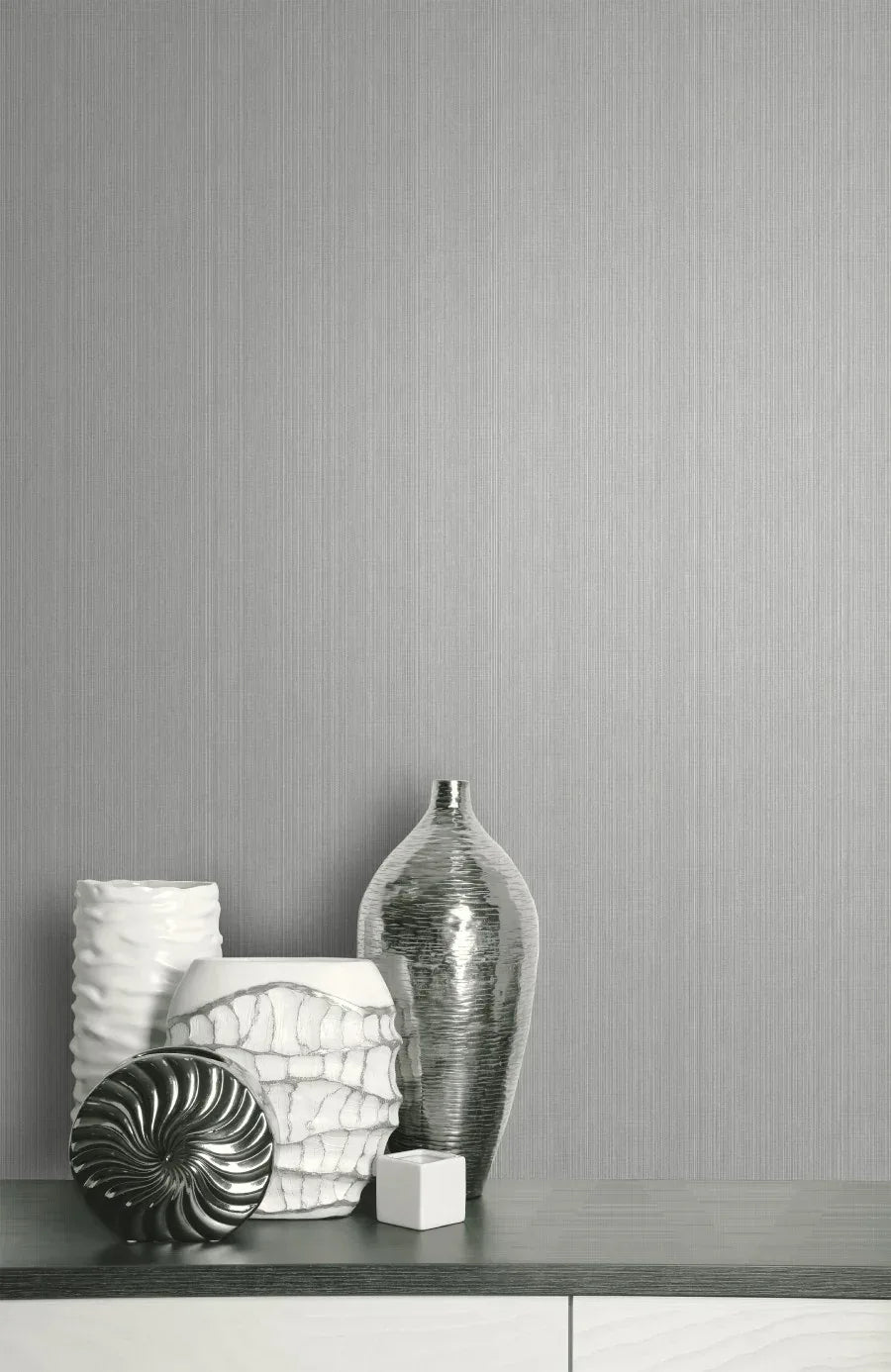 Five white and silver decorative vases on a grey surface with Textile Vertical Wallpaper in the background.