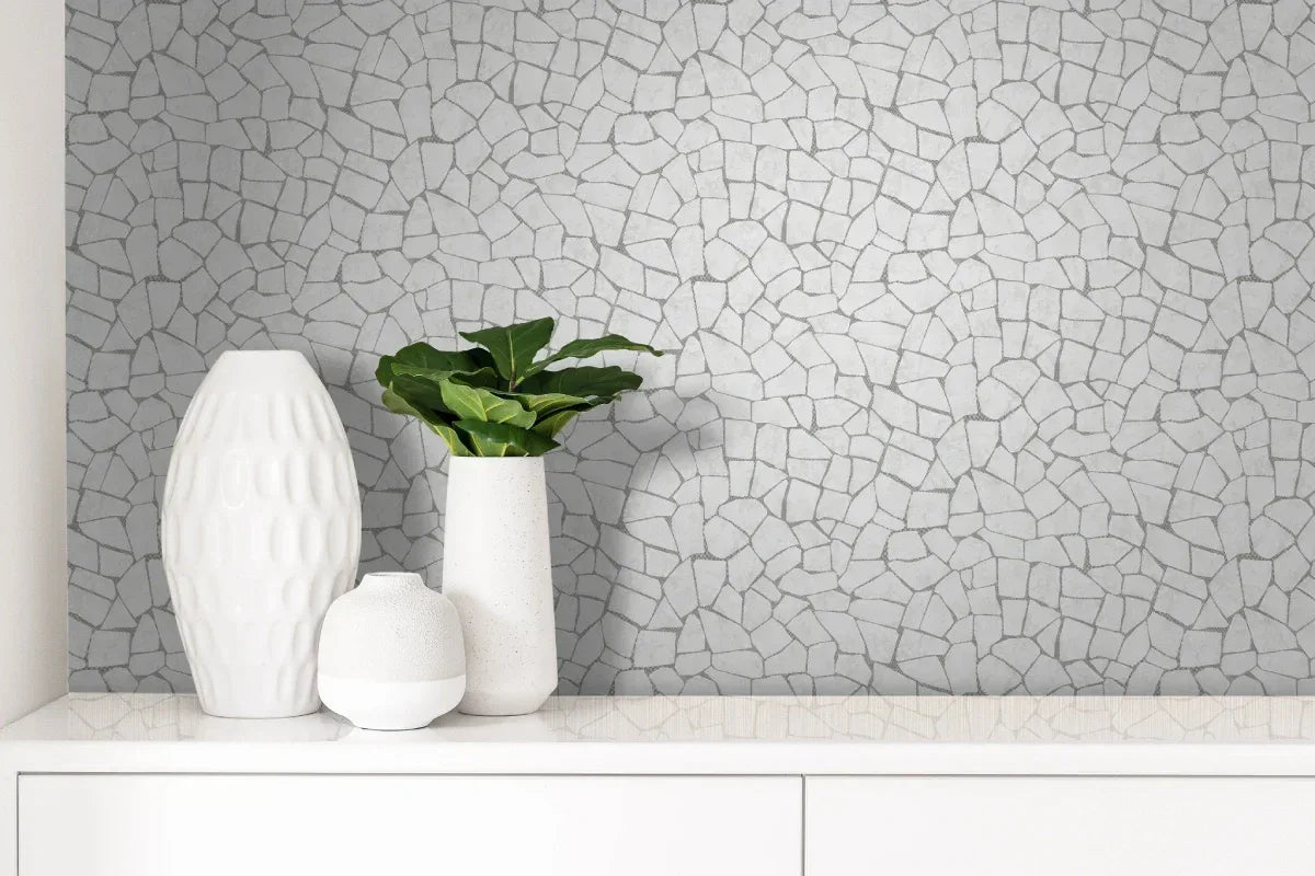 Three white vases and a green plant sit on a cabinet before a Skin Effect Wallpaper mosaic-patterned wall.