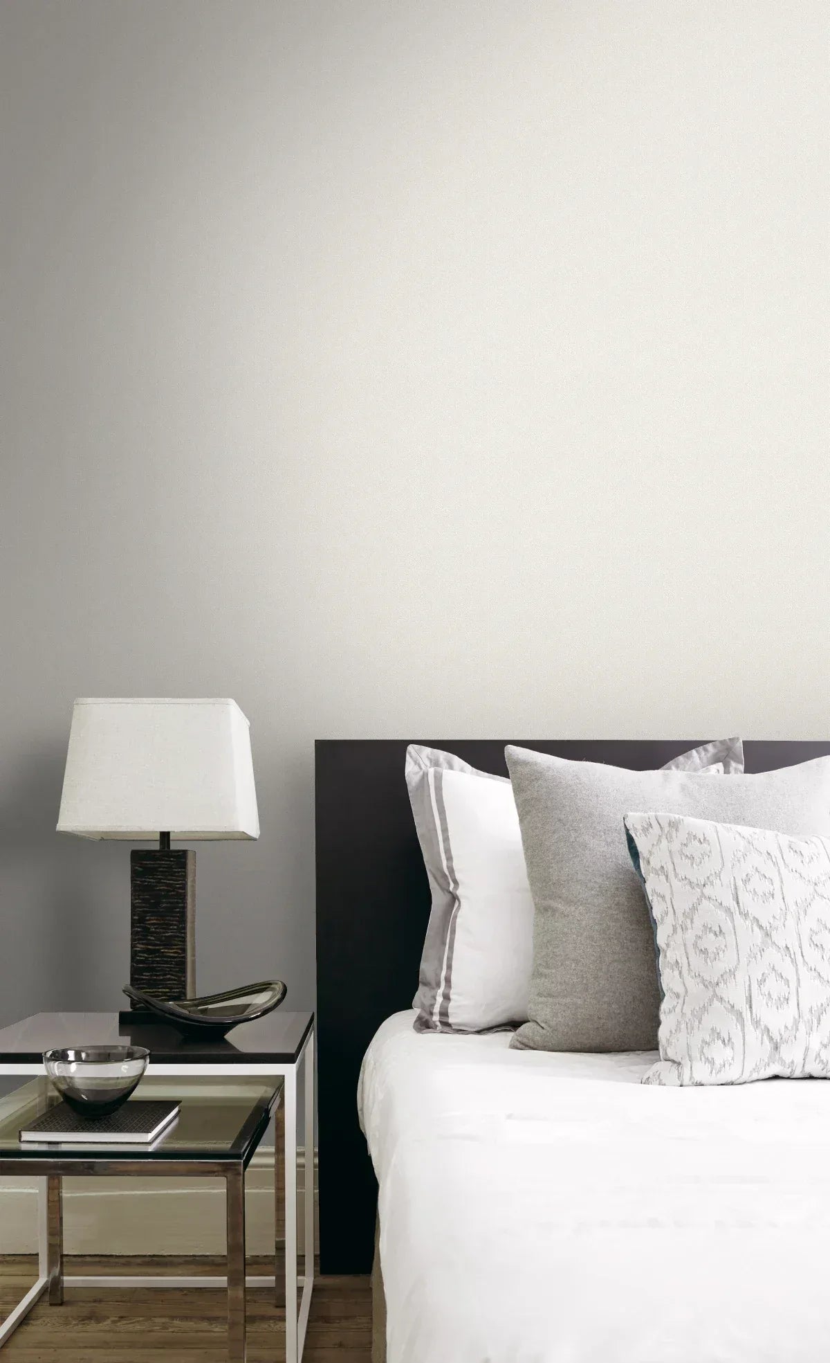 Modern bedroom with a black headboard, white bedding, gray pillows, and Breeze Plain Texture Wallpaper behind the nightstand.