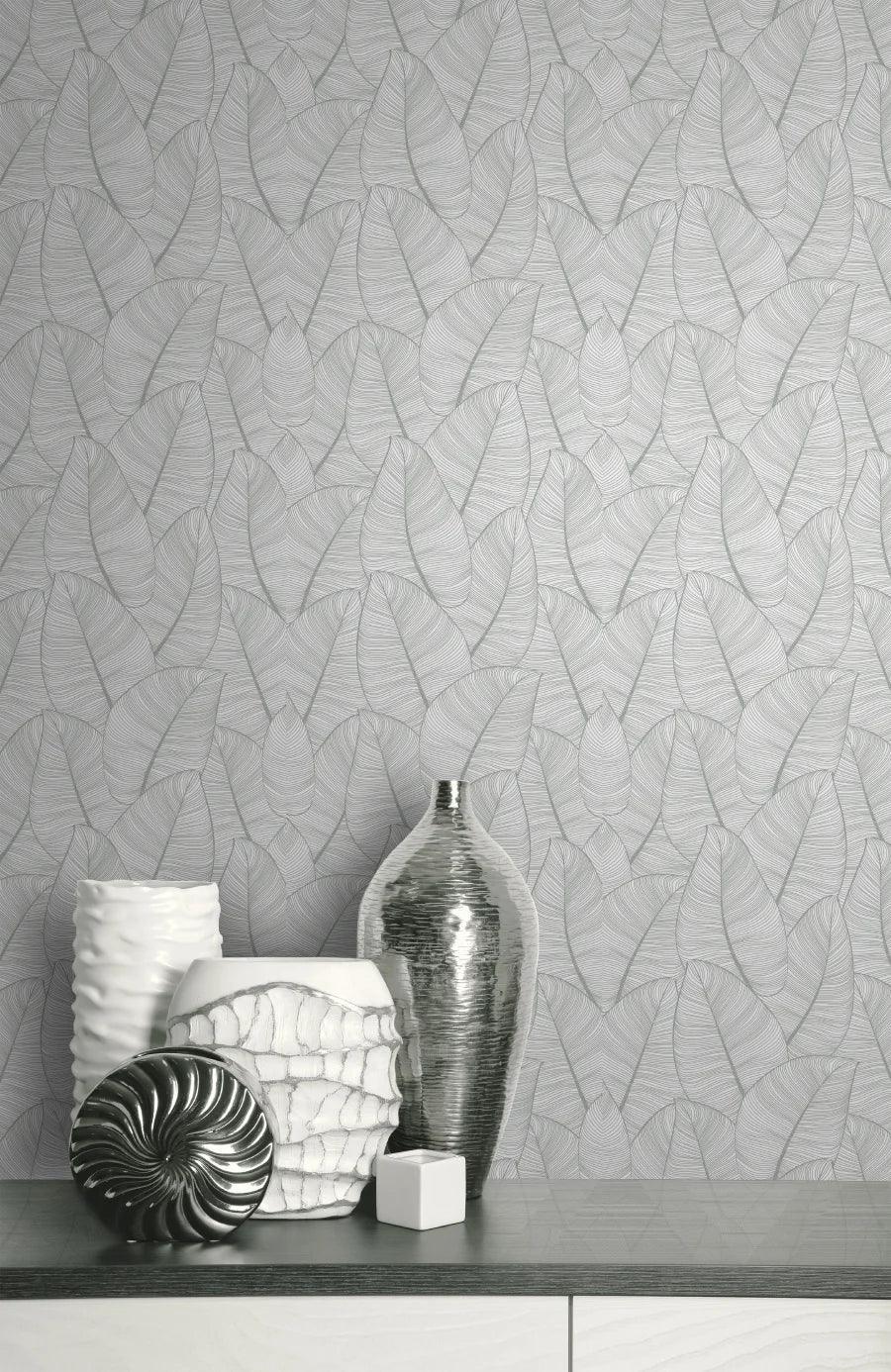 Silver and white ceramic vases on a countertop accent metallic leaf wallpaper with a subtle gray pattern.