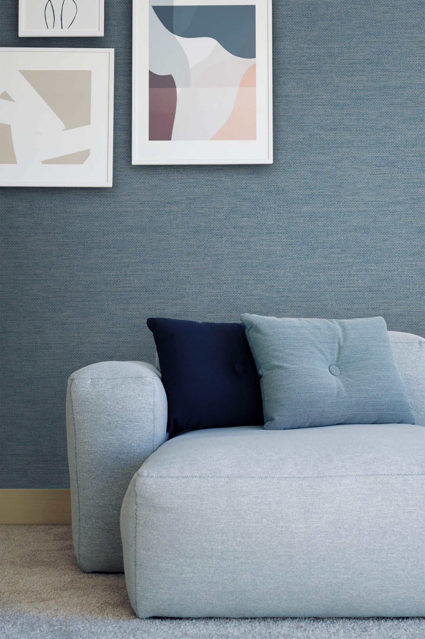 Light blue sofa with navy cushions set against Texture Effect Wallpaper, beneath abstract framed artwork.