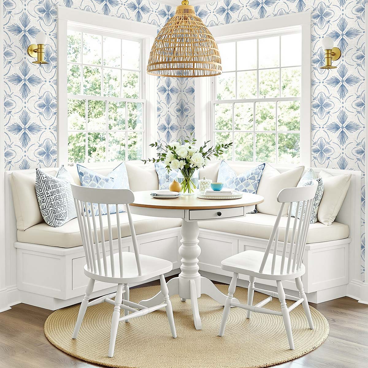 Bright breakfast nook with a round table, white chairs, built-in bench, and blue Tropical Bali Essence wallpaper.