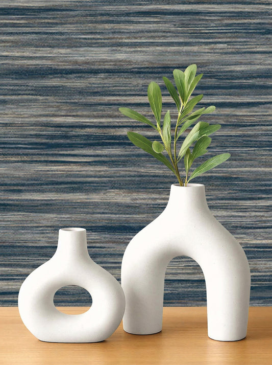 Two modern white ceramic vases sit on wood against Faux Grasscloth Commercial Vinyl wallpaper with blue stripes.