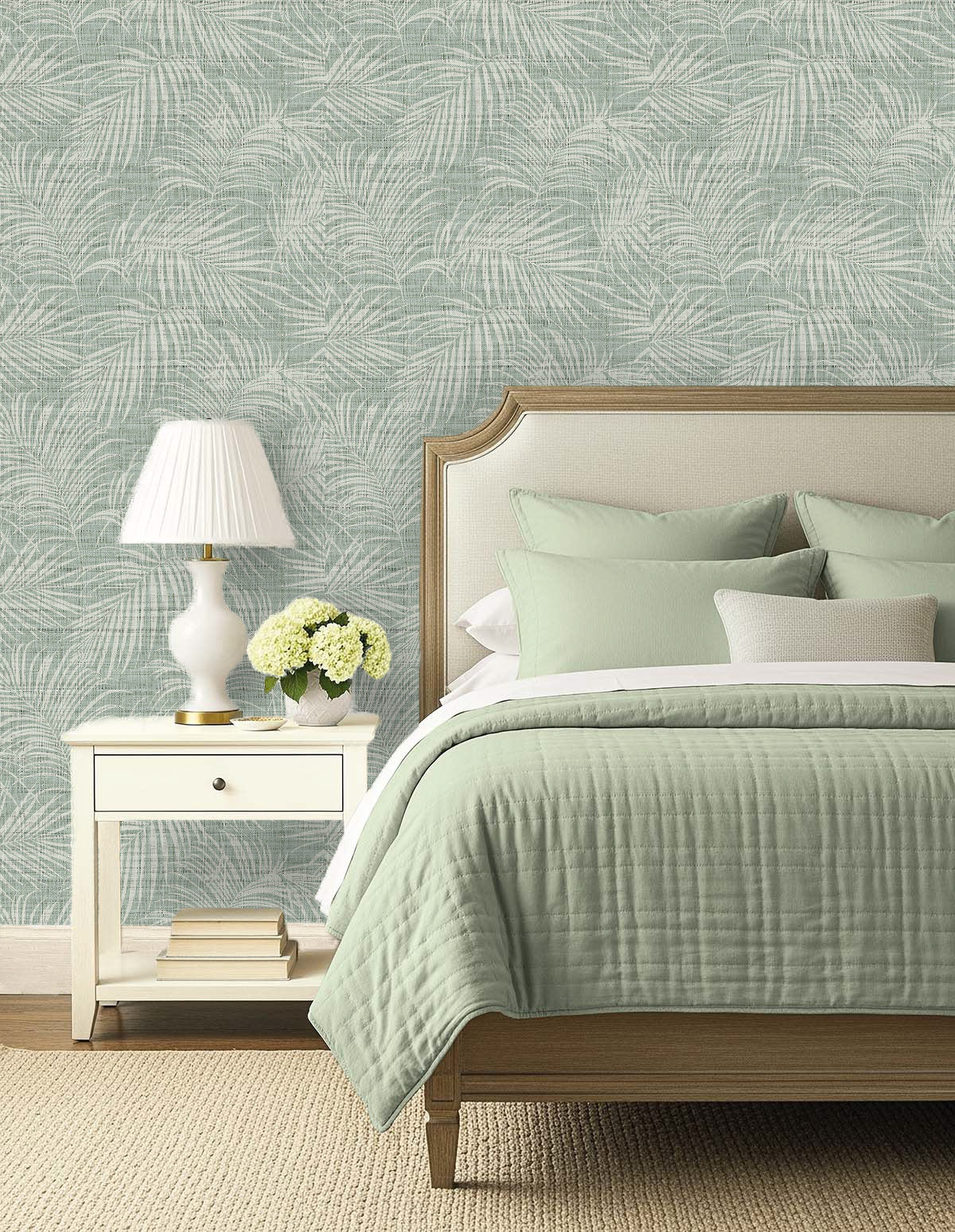 A bed with sage green bedding and a white nightstand sits against Palm Grassland Commercial Vinyl wallpaper.