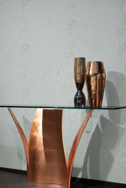 A glass table with a sculptural copper base holds two metallic vases before Algarve Cork Grasscloth Naturals.