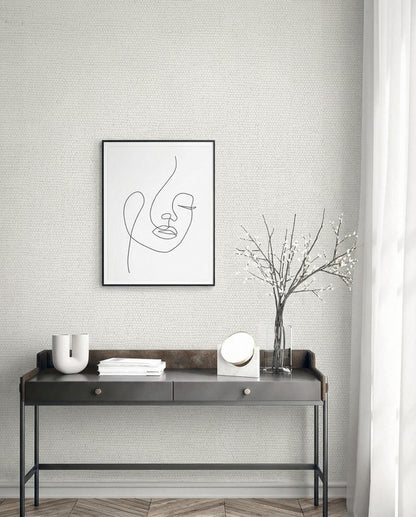 Minimalist room with a black metal console, abstract face art, and Grasscloth Texture Grasscloth Naturals wallpaper.