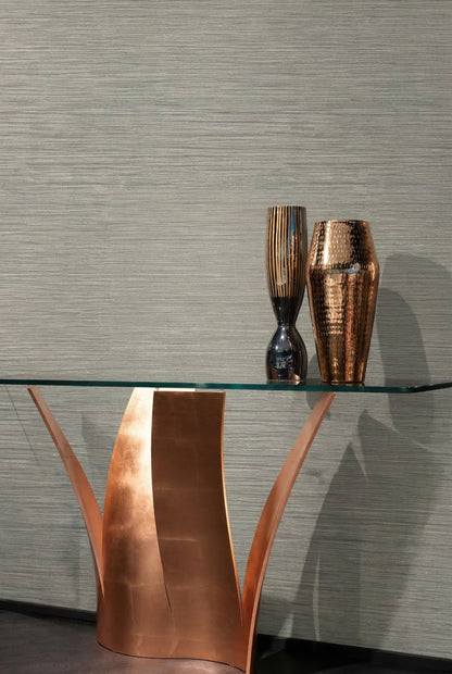 A glass table with a copper base stands before Grasslands Commercial Vinyl wallcovering in textured gray.