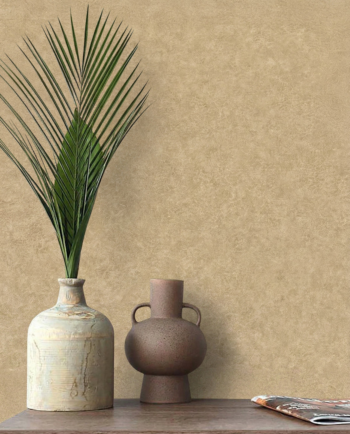 A palm leaf in a ceramic vase and brown jug rest on a table with Florence Leather Commercial Vinyl wallpaper backdrop.