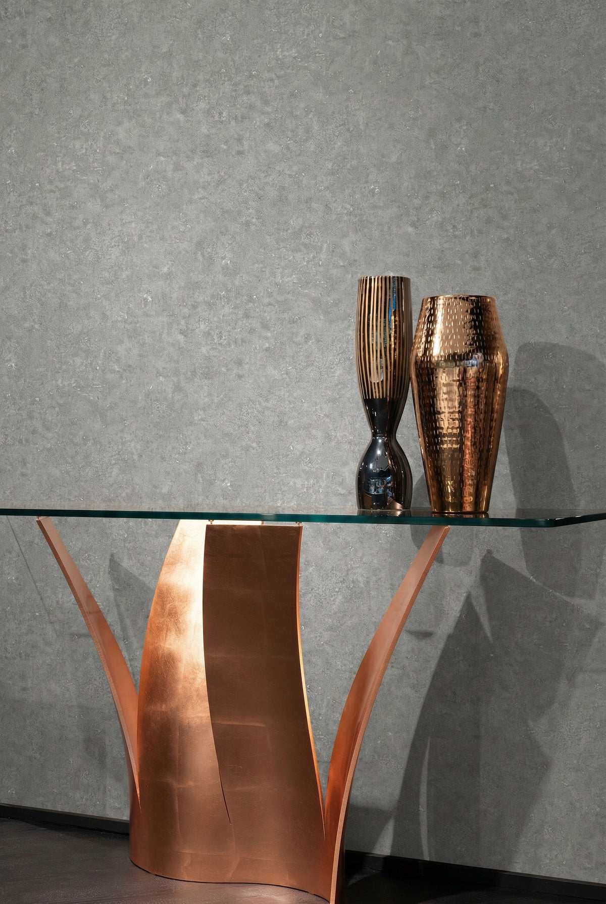 A glass table with a copper base sits before Florence Leather Commercial Vinyl, holding two metallic vases.
