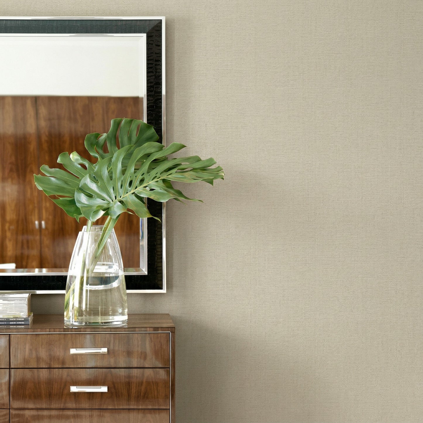 A clear glass vase with green leaves sits on a dresser beneath a mirror and Faux Paperweave Commercial Vinyl wallpaper.