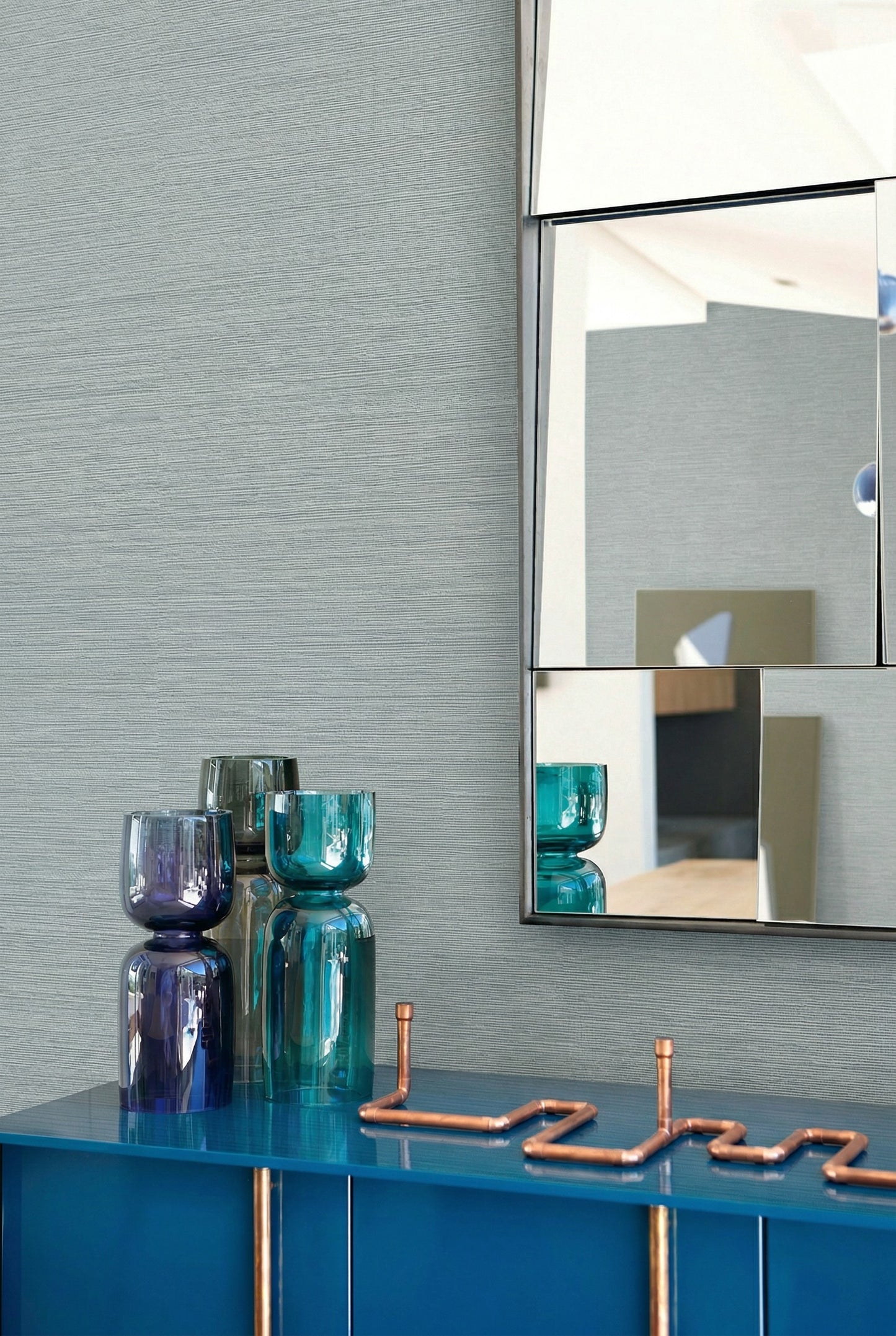 Blue vases and a zigzag copper accent sit on a blue cabinet beside Sisal Texture Grasscloth Naturals wallpaper.