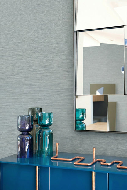 Blue vases and a zigzag copper accent sit on a blue cabinet beside Sisal Texture Grasscloth Naturals wallpaper.