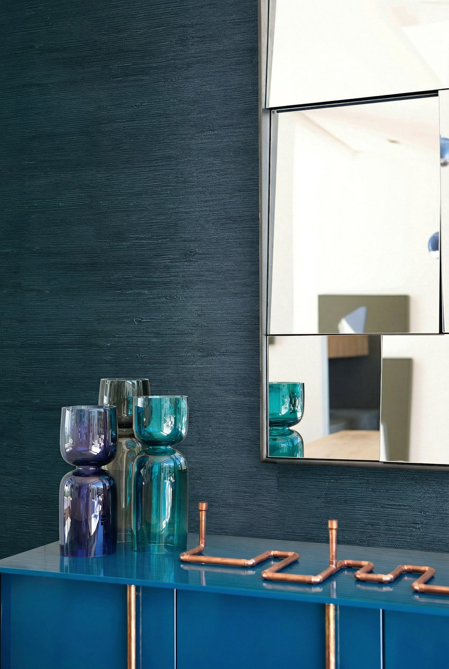 Modern decor with glass vases on a blue cabinet and a geometric mirror on Straw Texture Grasscloth wallcovering.