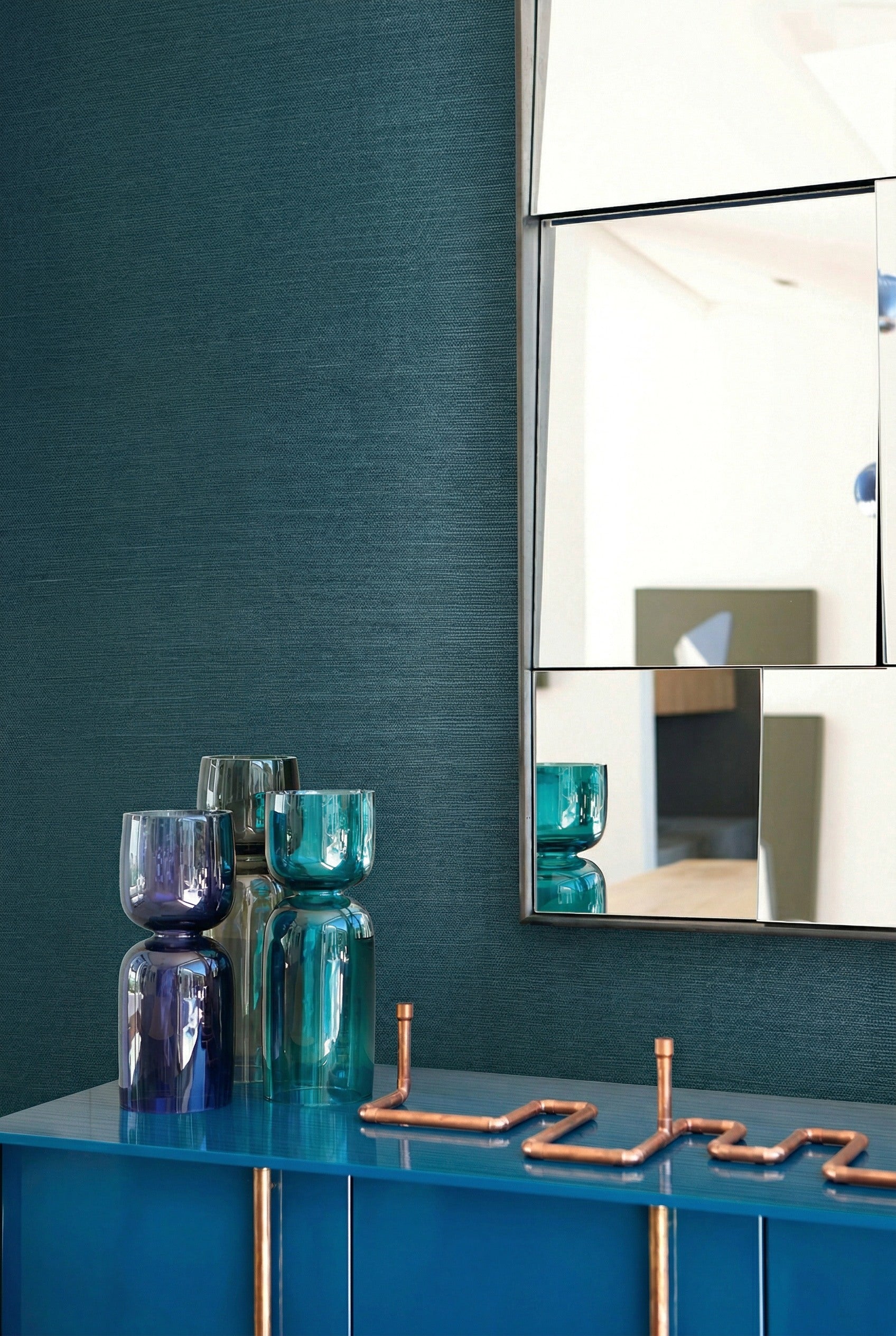 Blue and green glass vases on a blue cabinet beneath a geometric mirror on Sisal Texture Grasscloth Naturals.