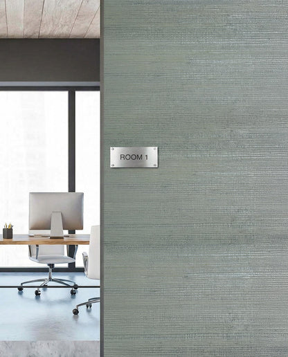 A modern office with a desk and chair sits by a ROOM 1 wall sign featuring Sisal Texture Grasscloth Naturals wallpaper.