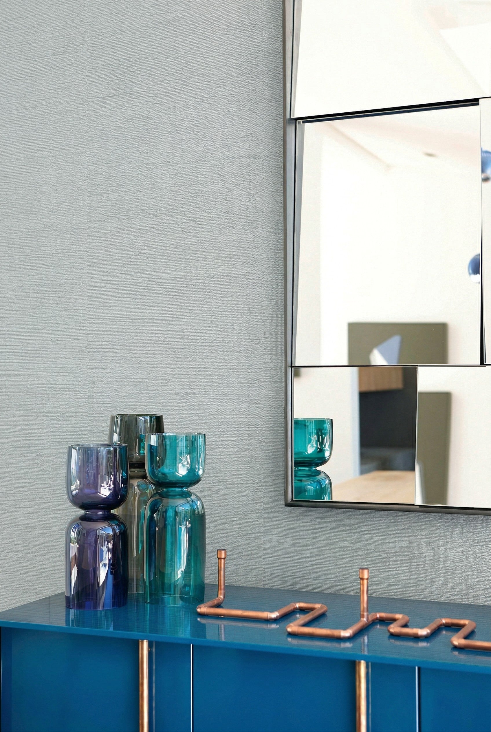 Modern decor with blue glass vases, a geometric mirror, and Sisal Texture Grasscloth Naturals wallpaper.