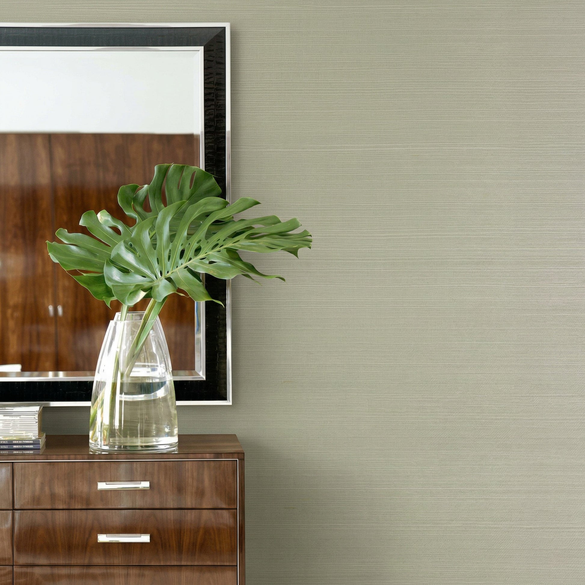 Large green monstera leaves in a clear vase on a wood dresser, with Sisal Texture Grasscloth Naturals on the wall.