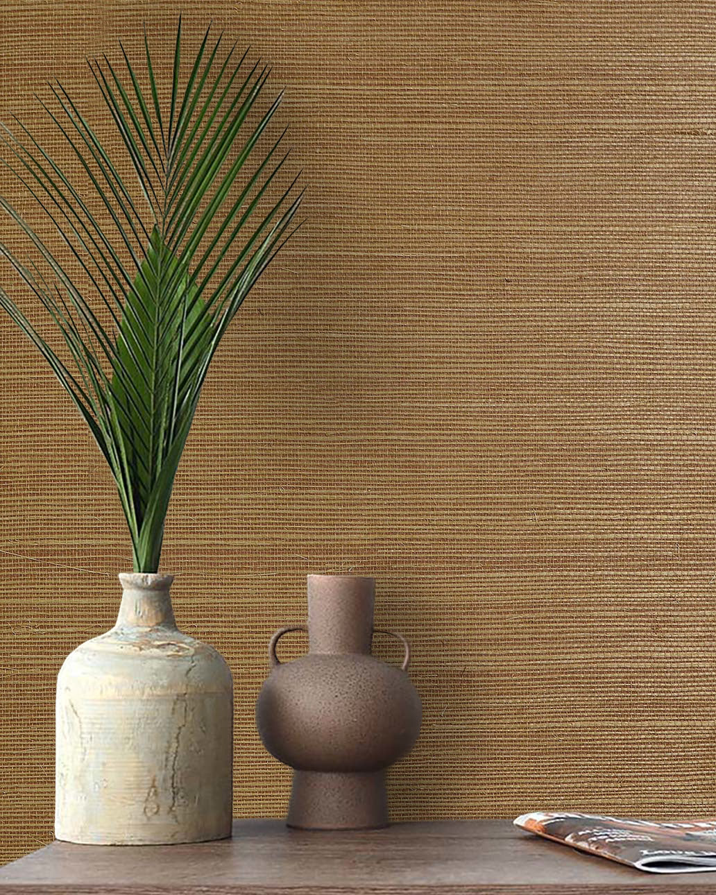 Two ceramic vases with a palm leaf sit on a table, set against Sisal Texture Grasscloth Naturals wallcovering.