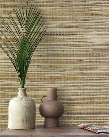 A ceramic vase with a palm leaf and a jug sit on wood against Straw Texture Grasscloth Naturals wallcovering.