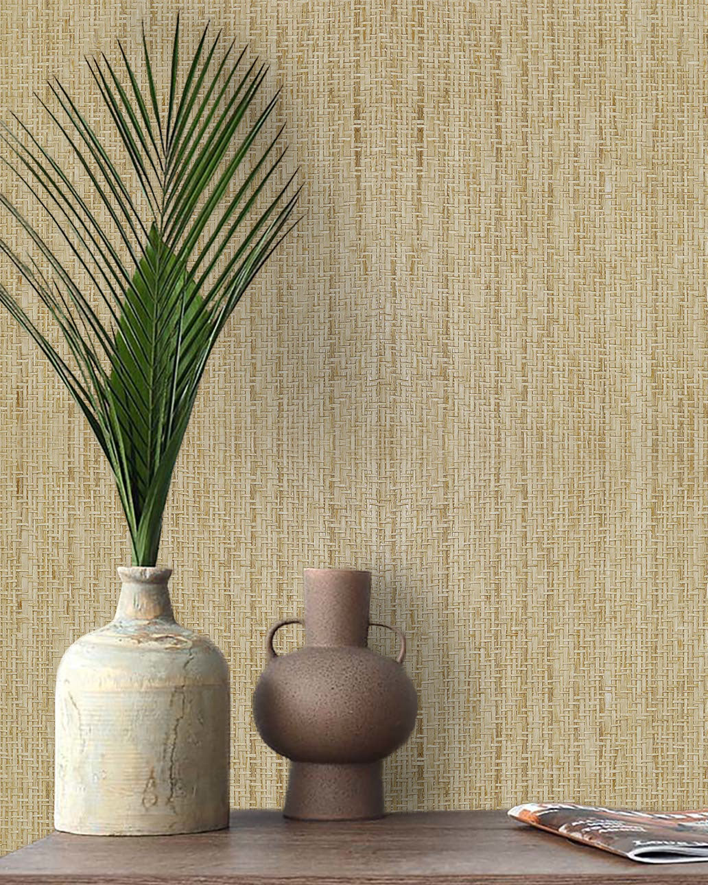 A palm leaf in a ceramic vase and a jug sit on a wooden table against Paper Interlace Texture Grasscloth Naturals.