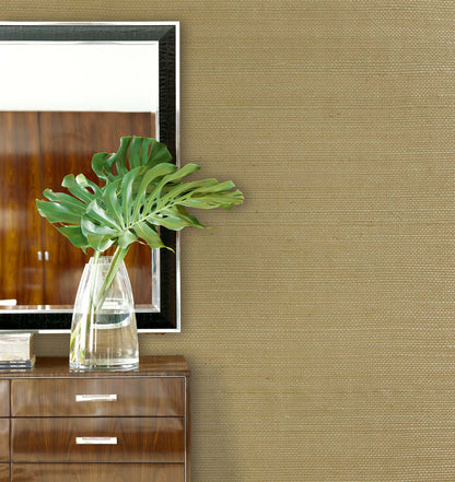Large green leaves in a clear vase sit on a dresser below a mirror with Sisal Texture Grasscloth Naturals wallpaper.