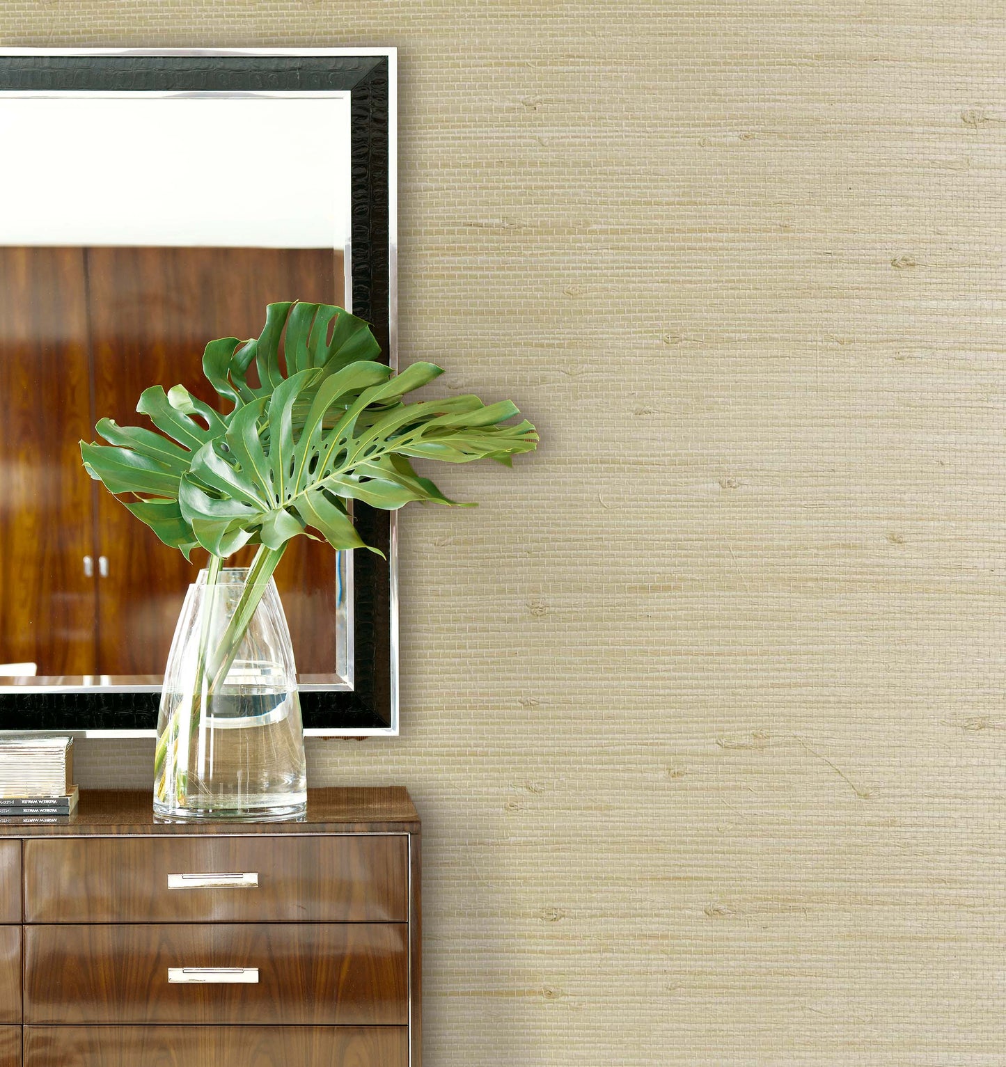 A clear glass vase with green leaves sits on a wooden dresser beside Straw Texture Grasscloth Naturals wall decor.