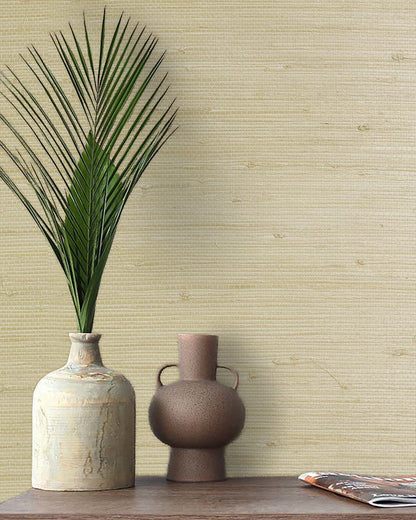 A palm leaf in a ceramic vase and a brown jug on a wooden table with Straw Texture Grasscloth Naturals wall decor.