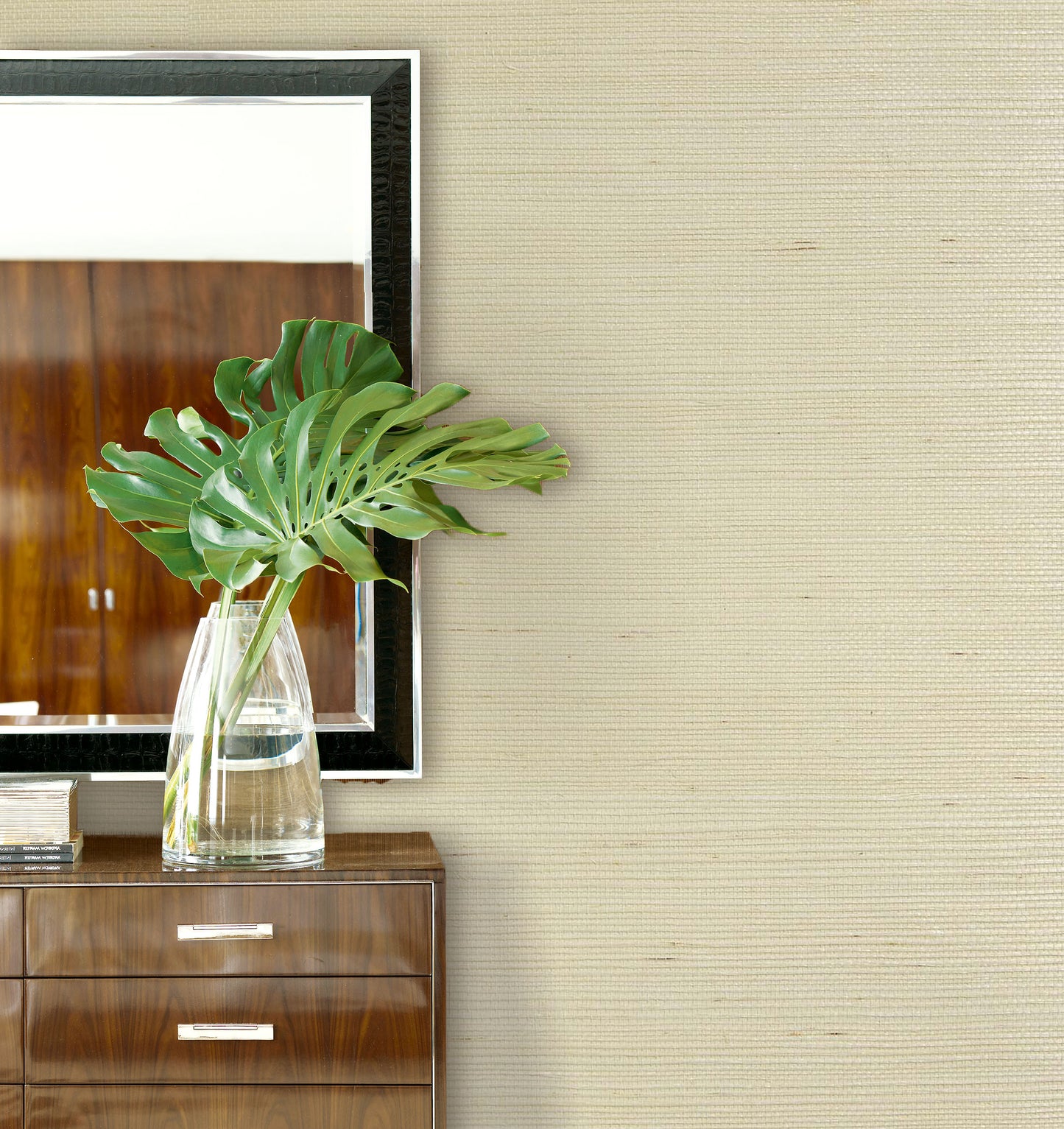 Green leaves in a glass vase on a cabinet, next to a mirror and Sisal Texture Grasscloth Naturals on the wall.