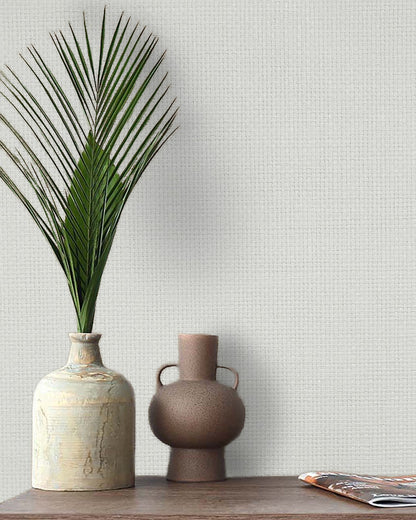 Two ceramic vases, one with a palm frond, sit by a magazine and Paperbraid Texture Grasscloth Naturals wallpaper.