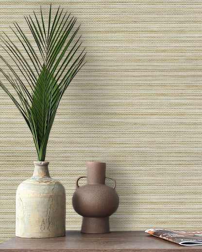 A ceramic vase with palm fronds and a small jug sit on a wooden table against Straw Texture Grasscloth Naturals.