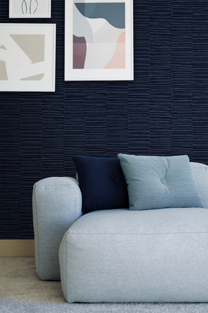 Gray sofa with blue and black cushions against a wall decorated with Blue Industrial Grasscloth Stripe Commercial & Vinyl with framed abstract art.