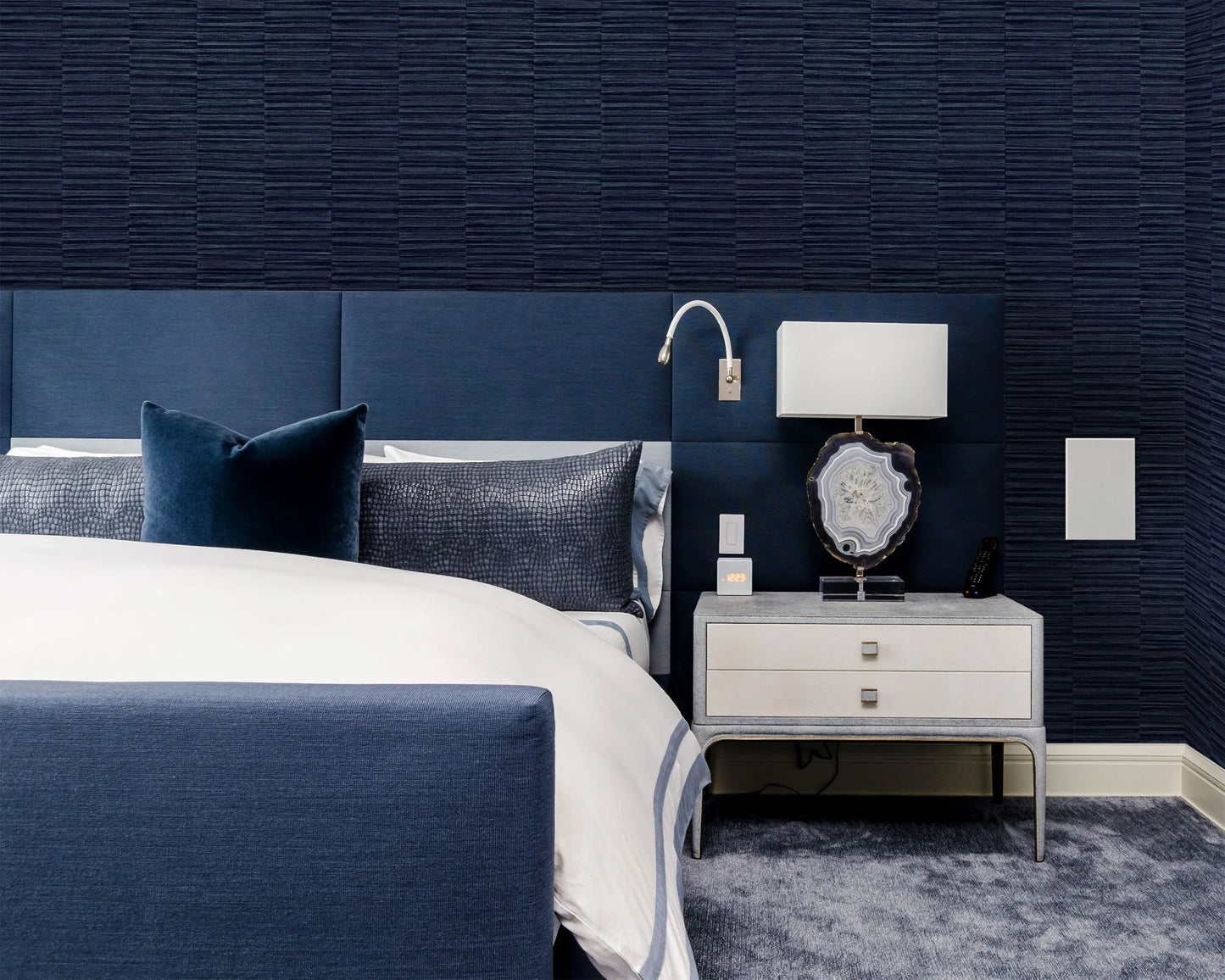 Modern bedroom with a navy bed, white bedding, and an accent wall in Industrial Grasscloth Stripe Vinyl wallpaper.